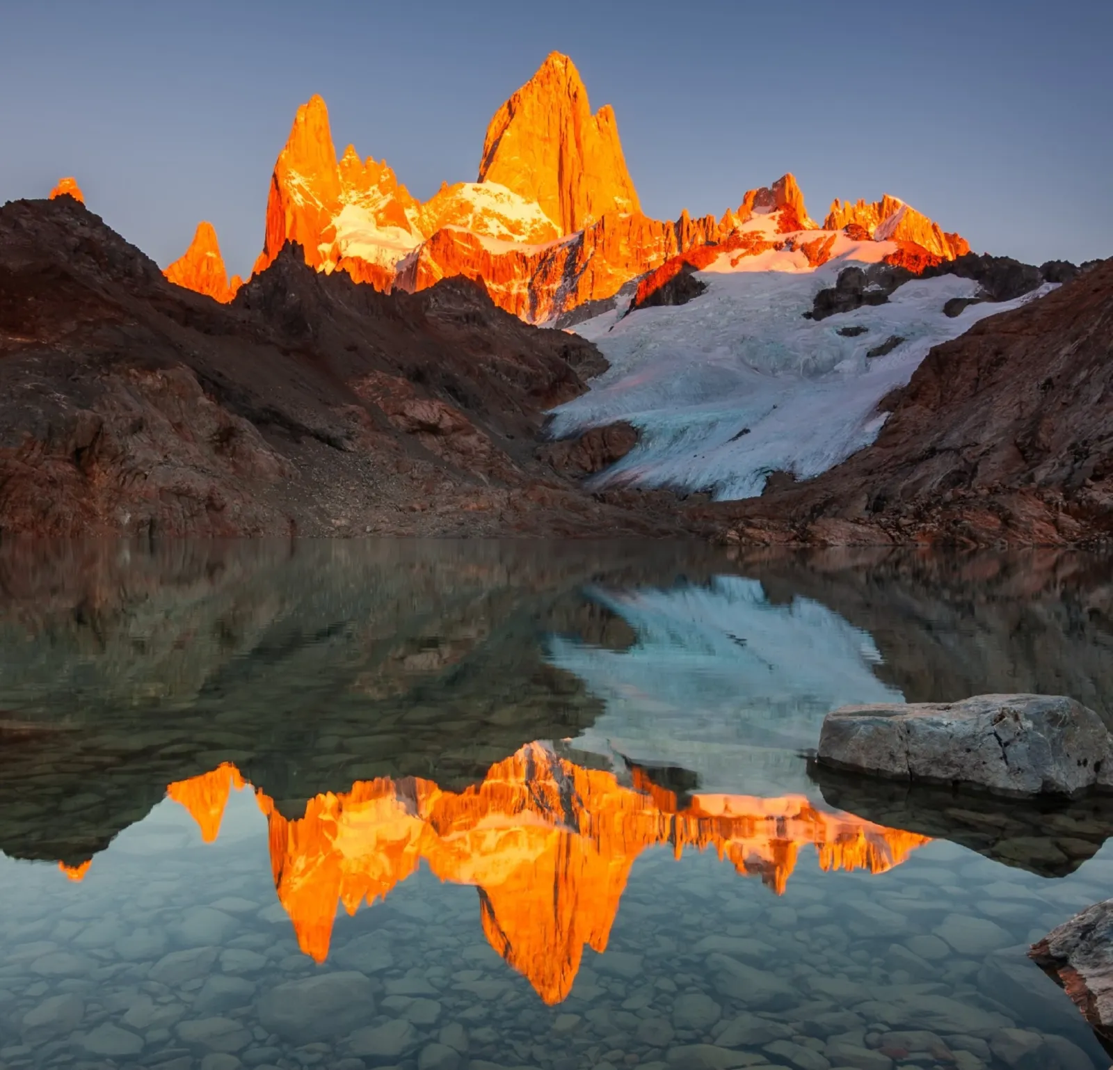 El Monte Chaltén encendido por la primera luz del día, reflejado en una laguna