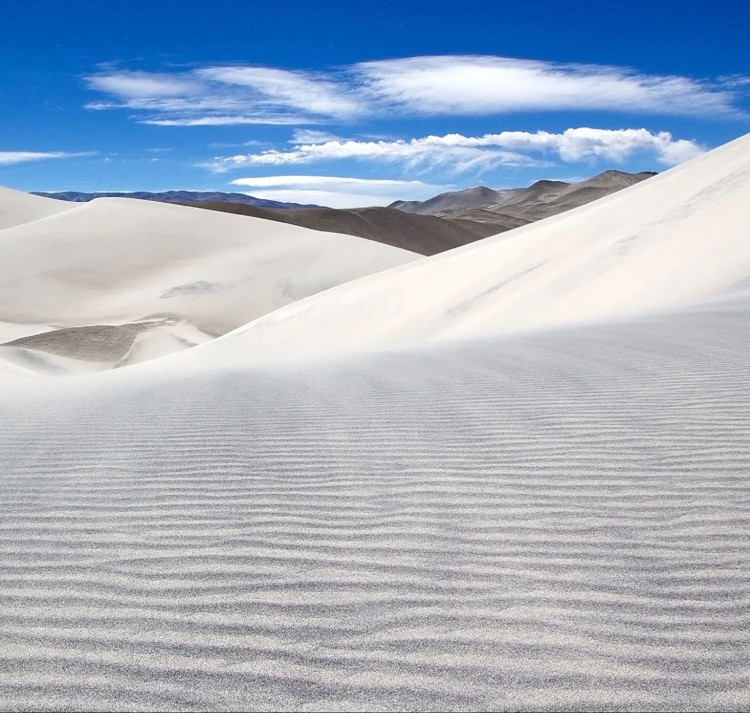 Duna de arena blanca bajo un cielo azul con nubes