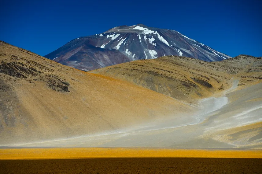 Volcán nevado sobre laderas doradas de la puna