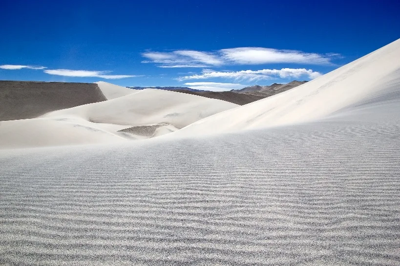 Duna de arena blanca con ondulaciones del viento bajo un cielo con nubes