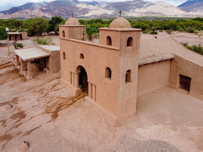Iglesia de adobe con dos torres y cúpulas, con cerros de fondo